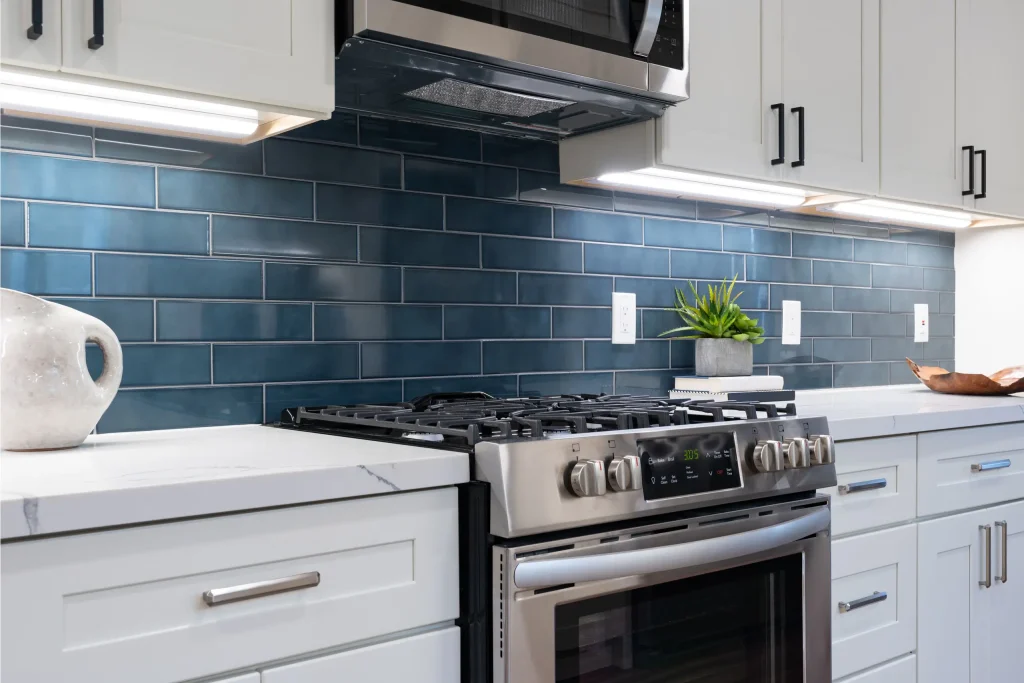 Modern kitchen details of white marble counter, gas stove, and blue tile backsplash.