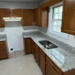 Modern kitchen with granite countertops and natural wood cabinetry.